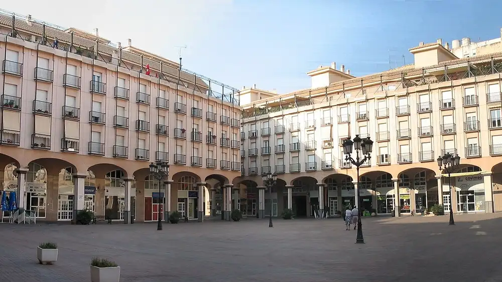 Plaza Mayor de Elda, con edificios de varias plantas y soportales alrededor de una plaza peatonal con farolas