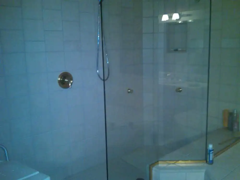 Ducha de obra con mampara de cristal, grifería empotrada y paredes alicatadas en blanco