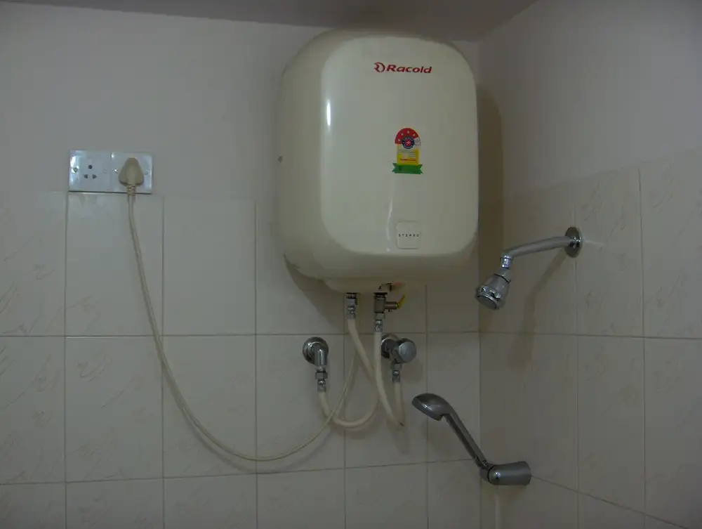Termo eléctrico blanco colgado en la pared de un baño alicatado, con su toma de corriente y los tubos de agua
