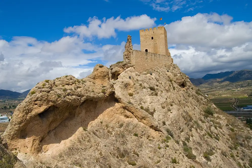 Castillo de Sax en lo alto de un peñasco de roca, con el valle y las sierras al fondo